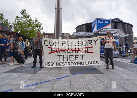 Londres, Royaume-Uni. 05 août 2021. Les manifestants tiennent une bannière anti-HS2 à côté d'un guichet d'information Euston HS2 lors de l'arrêt de la manifestation HS2.les activistes se sont rassemblés devant la gare de King's Cross pour protester contre le nouveau système ferroviaire High Speed 2 (HS2), qui selon les écologistes sera « écologiquement dévastateur » et coûtera aux contribuables 170 milliards de livres sterling. Crédit : SOPA Images Limited/Alamy Live News Banque D'Images