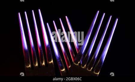 Gros plan de trois fourches brillantes sur un fond noir éclairé par des lumières colorées faisant une image abstraite Banque D'Images