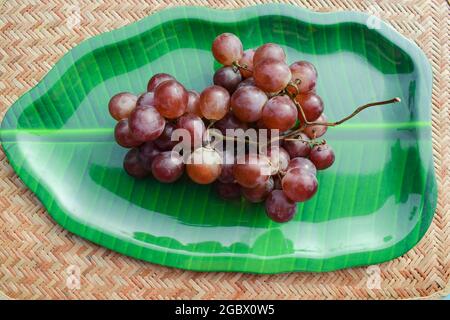 Beau bouquet de raisins rouges de grandes raisins doux avec tige importée en Inde asie. Raisins servis sur plateau de feuilles Banque D'Images