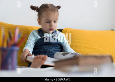 Deux enfants avant-garçonnets lisent un grand livre intéressant de contes de fées sur un lit jaune. Frères et sœurs petits jumeaux lecteur ont plaisir, heureux enfant sur Banque D'Images