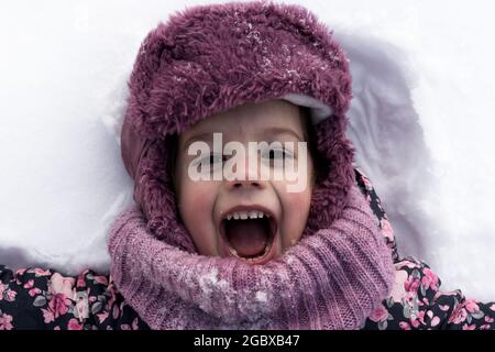 Concepts d'hiver, de famille, d'enfance - portrait en gros plan petite fille authentique d'âge préscolaire en vêtements roses sourire rire crier avec la bouche ouverte sur Banque D'Images