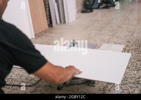 disque électrique coupant une planche blanche qui est tenue par un homme adulte dans un atelier Banque D'Images