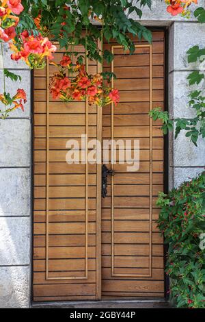 Ancienne porte en bois faite de planches horizontales étroites et de belles fleurs d'orange au-dessus. Banque D'Images