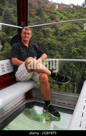 Vue sur la terre à travers le plancher de verre d'une cabine Crystal. Homme dans la cabine de téléphérique avec plancher en verre. Promenades touristiques sur la télécabine. Genting Highland Banque D'Images