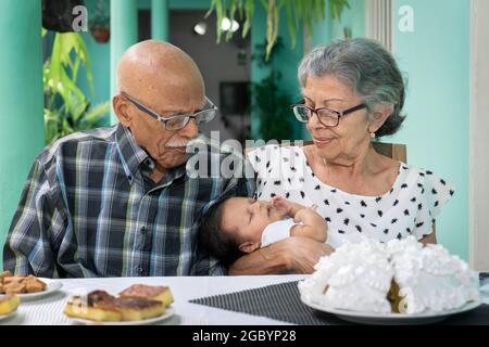 Couple âgé assis à une table avec un bébé dans les bras de la femme Banque D'Images