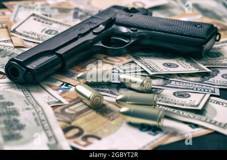 Pistolet et balles sur le fond des billets en dollars et en euros, vue rapprochée. Argent criminel. Argent noir et protection, mafia et corruption concept, Banque D'Images