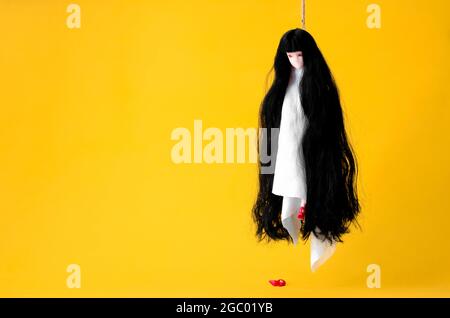 Cheveux longs asiatique femelle fantôme suspendu avec la corde agissant suicide sur fond orange. Concept effrayant pour Halloween minimal. Banque D'Images