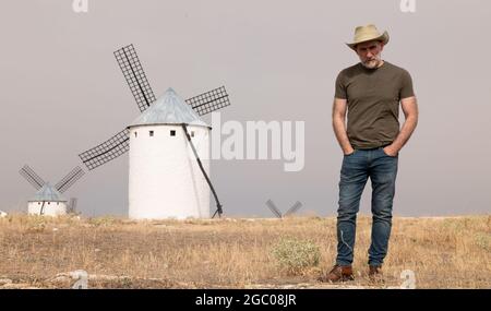 Un homme portant un chapeau de cow-boy avec des moulins à vent dans la campagne Banque D'Images