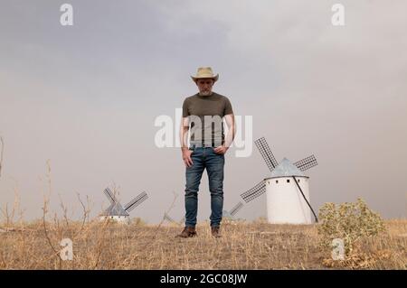 Un homme portant un chapeau de cow-boy avec des moulins à vent dans la campagne Banque D'Images