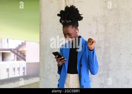 Femme africaine portant des écouteurs sans fil, sélectionnant la musique avec son téléphone. Banque D'Images