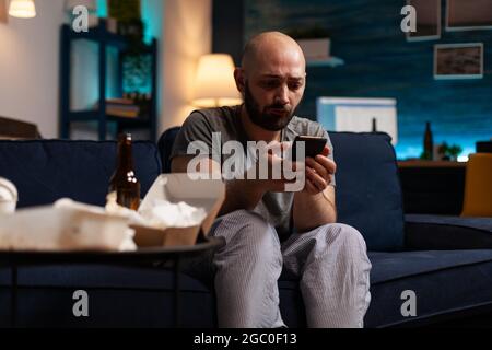 Triste malheureux désespéré désespéré anxiété choquée homme naviguant sur smartphone, luttant avec la santé mentale passant par une dépression majeure de solitude. Frustré, contrarié, un homme a lu des factures numériques non payées Banque D'Images