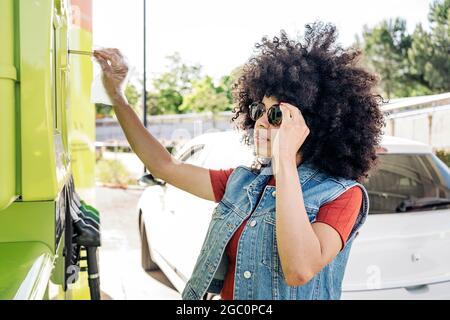 Belle femme aux cheveux d'afro payant avec sa carte de crédit après avoir rempli sa voiture d'essence à la station-service. Banque D'Images