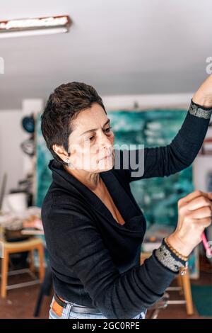 Peintre féminin concentré travaillant dans une grande toile avec une peinture colorée. Elle a un studio d'art dans son garage. Banque D'Images