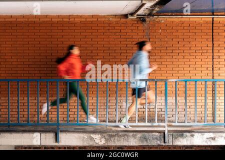 Des amis non reconnus portant des vêtements de sport courant dans la ville pendant les jours de pluie. Ils sont concentrés et regardent à l'avant. Banque D'Images