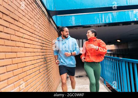 Jeunes amis portant des vêtements de sport courant à l'extérieur pendant les jours de pluie. Ils sont souriants et se regardent les uns les autres. Banque D'Images