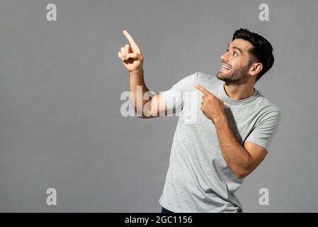 Portrait d'un jeune caucasien surpris avec les mains pointant vers le haut dans un arrière-plan isolé gris clair studio Banque D'Images