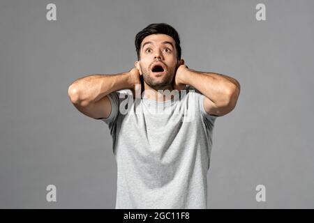 Un jeune homme du Caucase choqué se gazoulait avec les mains autour du cou en regardant vers le haut sur fond gris clair de studio Banque D'Images