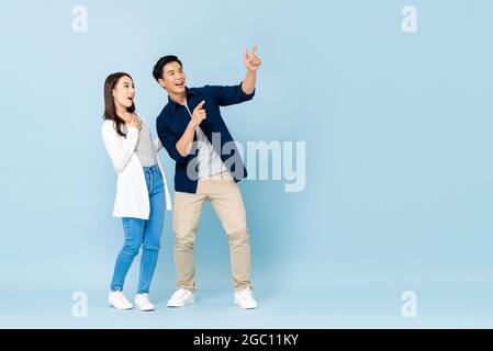 Portrait en longueur de touristes heureux de couple d'Asie excités pointant les mains vers l'espace vide sur fond bleu clair isolé Banque D'Images