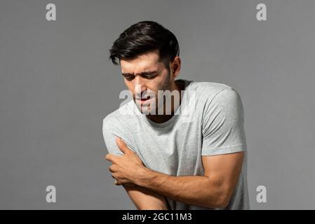 Jeune homme caucasien souffrant de douleurs à l'épaule, prise en studio sur fond gris isolé Banque D'Images