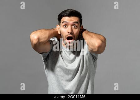 Un jeune caucasien choqué se gazoulait avec les mains autour du cou en regardant la caméra sur fond gris clair de studio Banque D'Images