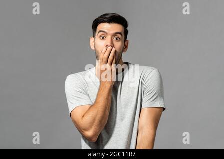 Portrait d'un jeune caucasien choqué avec une bouche couvrant la main sur fond gris clair de studio Banque D'Images