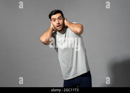 Surpris jeune homme caucasien souffle avec les mains derrière le cou sur fond gris clair isolé studio Banque D'Images