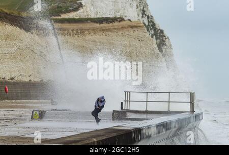 Brighton Royaume-Uni 6 août 2021 - UN marcheur est mouillé comme d'énormes vagues se brisent au-dessus de la promenade sous la falaise à Saltdean près de Brighton que d'autres tempêtes battent la côte sud aujourd'hui : Credit Simon Dack / Alay Live News Banque D'Images
