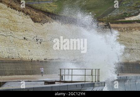 Brighton Royaume-Uni 6 août 2021 - UN coureur passe par d'énormes vagues au-dessus de la promenade sous la falaise à Saltdean près de Brighton que d'autres tempêtes battent la côte sud aujourd'hui : Credit Simon Dack / Alay Live News Banque D'Images