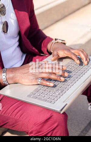 mains d'un africain méconnaissable travaillant avec son ordinateur portable assis sur un escalier dans la ville, concept de technologie et travail à distance Banque D'Images