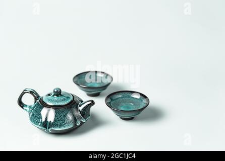 Thé vert dans une théière d'argile turquoise foncé et deux petites tasses sur fond pastel. Concept créatif minimaliste de cérémonie de thé. Copier l'espace. Banque D'Images