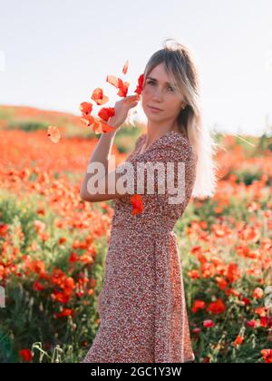 Belle femme blonde dans un champ de pavot au coucher du soleil. Concept de liberté avec des couleurs douces. Banque D'Images