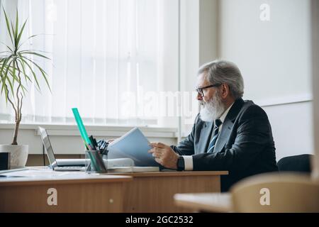 Portrait d'un homme âgé à tête grise, professeur, enseignant vérifiant les devoirs des élèves en classe, à l'intérieur. Concept de profession professionnelle, emploi Banque D'Images