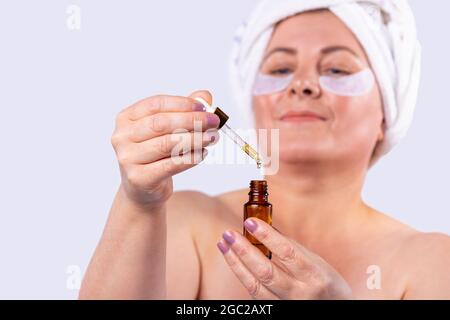 Gros plan d'une belle femme avec des mains bien entretenues et une manucure rose vif tenant une petite bouteille d'huile essentielle. Banque D'Images