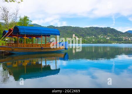 Bateau traditionnel de Pletna attendant les touristes sur le lac Bled, avec l'île du lac et charmante petite église en arrière-plan, les touristes célèbres atracti Banque D'Images