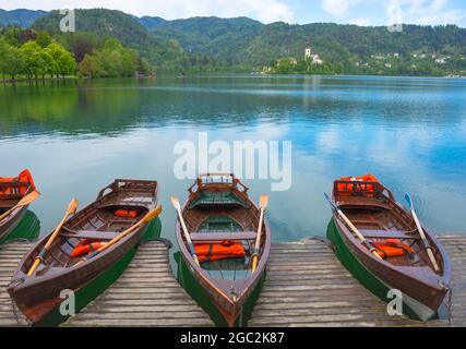 Des bateaux traditionnels attendent les touristes sur le lac Bled, avec l'île du lac et la charmante petite église en arrière-plan, célèbre attraction touristique dans Banque D'Images