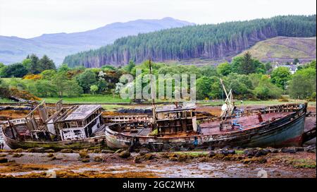 DES BATEAUX DE PÊCHE ABANDONNÉS COINCÉS DANS LA BOUE UN APRÈS-MIDI ENSOLEILLÉ, AVEC DE VASTES FORÊTS DE PINS ET DES MONTAGNES S'ÉTENDANT DERRIÈRE Banque D'Images