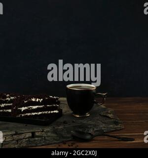 Tasse de café noir avec des morceaux de gâteau au chocolat et une cuillère sur une coupe en bois de chêne fissuré. Vue de dessus avec espace de copie d'arrière-plan bokeh bleu foncé Banque D'Images