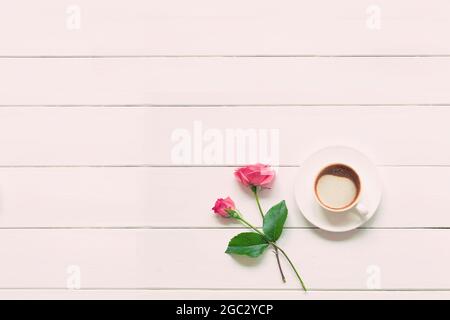 Une tasse de cappuccino chaud frais avec deux roses roses sur une table en bois blanc. Vue de dessus avec espace de copie, plan de travail. Banque D'Images