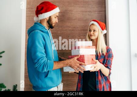 Un jeune homme donne une pile de cadeaux de Noël à une jolie fille blonde. Banque D'Images