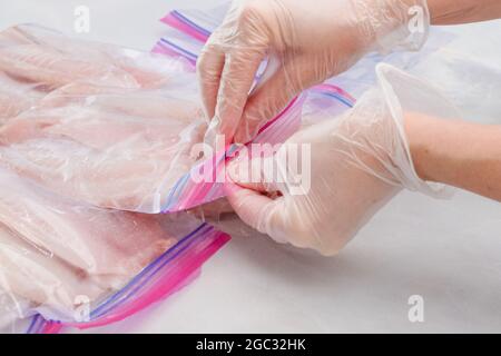 Les mains de femme mettent du filet de poisson frais Tilapia dans des sacs à fermeture à glissière pour geler, vue rapprochée Banque D'Images