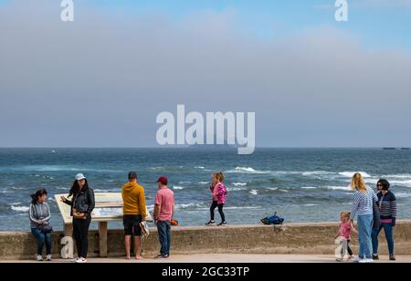 North Berwick, East Lothian, Écosse, Royaume-Uni, 6 août 2021. Météo au Royaume-Uni : journée brumeuse avant de fortes pluies : la ville est enveloppée de brouillard marin tandis que les gens marchent le long de la promenade. Photo : le Bass Rock est presque invisible de l'autre côté du Firth of Forth depuis Milsey Bay Banque D'Images