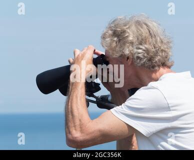 Un homme regarde intentement à travers une grande paire de jumelles soutenues sur un trépied.mains sont focalisation.mer et océan dans b Banque D'Images