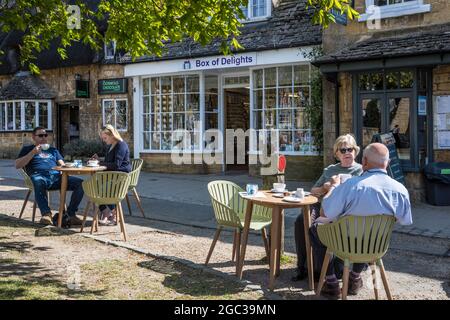 Les gens qui profitent du soleil de printemps, à l'extérieur d'un salon de thé dans la ville de Broadway, dans le Cotswold, dans le Worcestershire. Banque D'Images