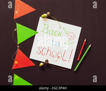 Carte de retour à l'école. Vacances, composition scolaire avec feuille blanche avec inspiration de retour à l'école, crayons, drapeaux en papier rouge et vert et une guirlande lumineuse Banque D'Images