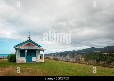 Au premier plan une chapelle blanche et bleue dans un pré, en arrière-plan les falaises de la côte espagnole et de la mer Cantabrique. Banque D'Images