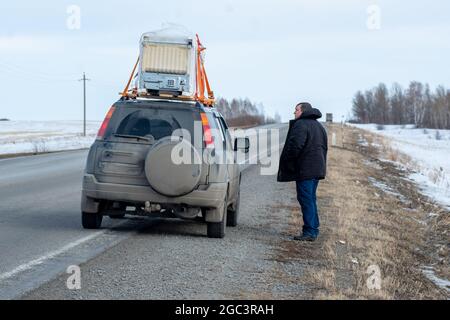 Un homme est debout à côté de la voiture, les gros bagages sont emballés sur le toit de voiture transport de cargaison surdimensionnée dans une petite voiture. Banque D'Images