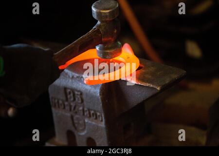 Travail dur dans le smithy sur l'enclume. Chaussure à cheval en acier brillant martelant. Forge forge un fer à cheval chaud Banque D'Images