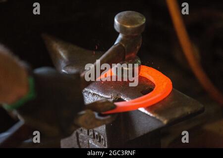 Travail dur dans le smithy sur l'enclume. Chaussure à cheval en acier brillant martelant. Forge forge un fer à cheval chaud Banque D'Images