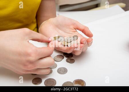 Économiser de l'argent, une main met des pièces dans une autre main, sur une table lumineuse sont des pièces de différents pays, gros plan. Banque D'Images