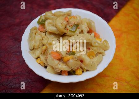 Gros plan de macaroni aux légumes cuits dans de la sauce blanche servi dans un bol transparent isolé sur fond blanc. Pâtes cuites à la carotte, au maïs, en capsule Banque D'Images